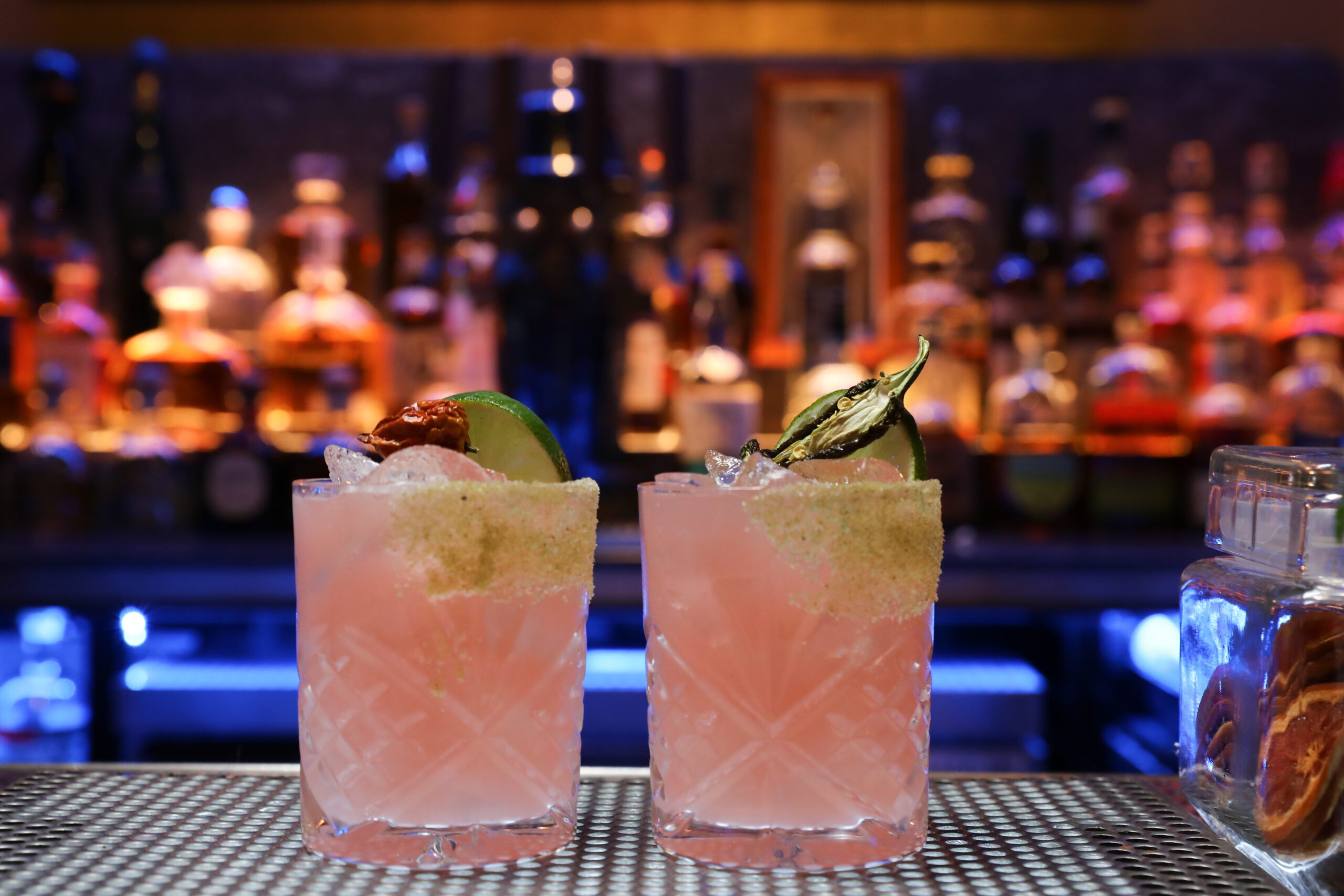 Two light pink coloured cocktails with the bar in the background.