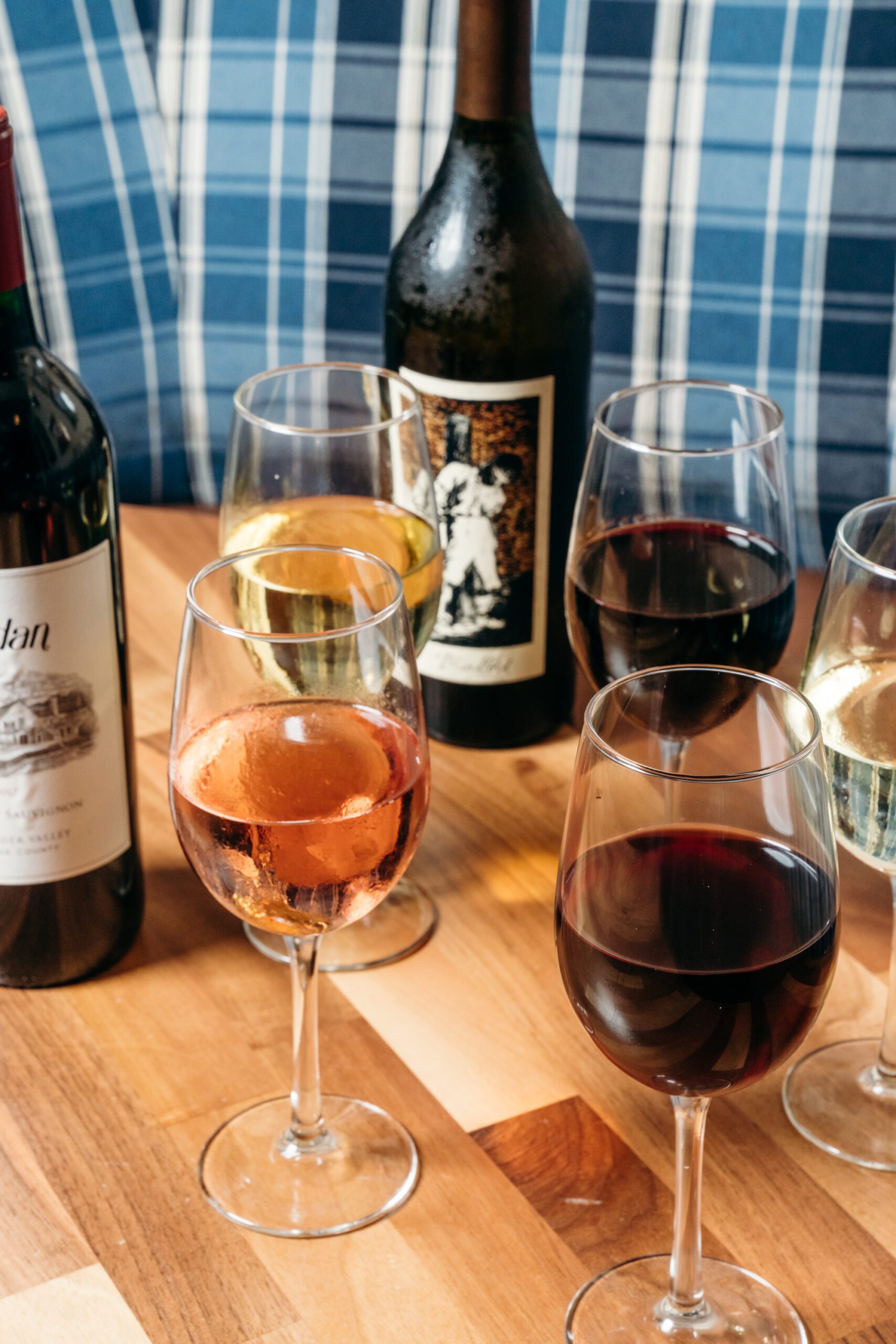 A couple of bottles of wine and five glasses of red, white and rose wine on a table.
