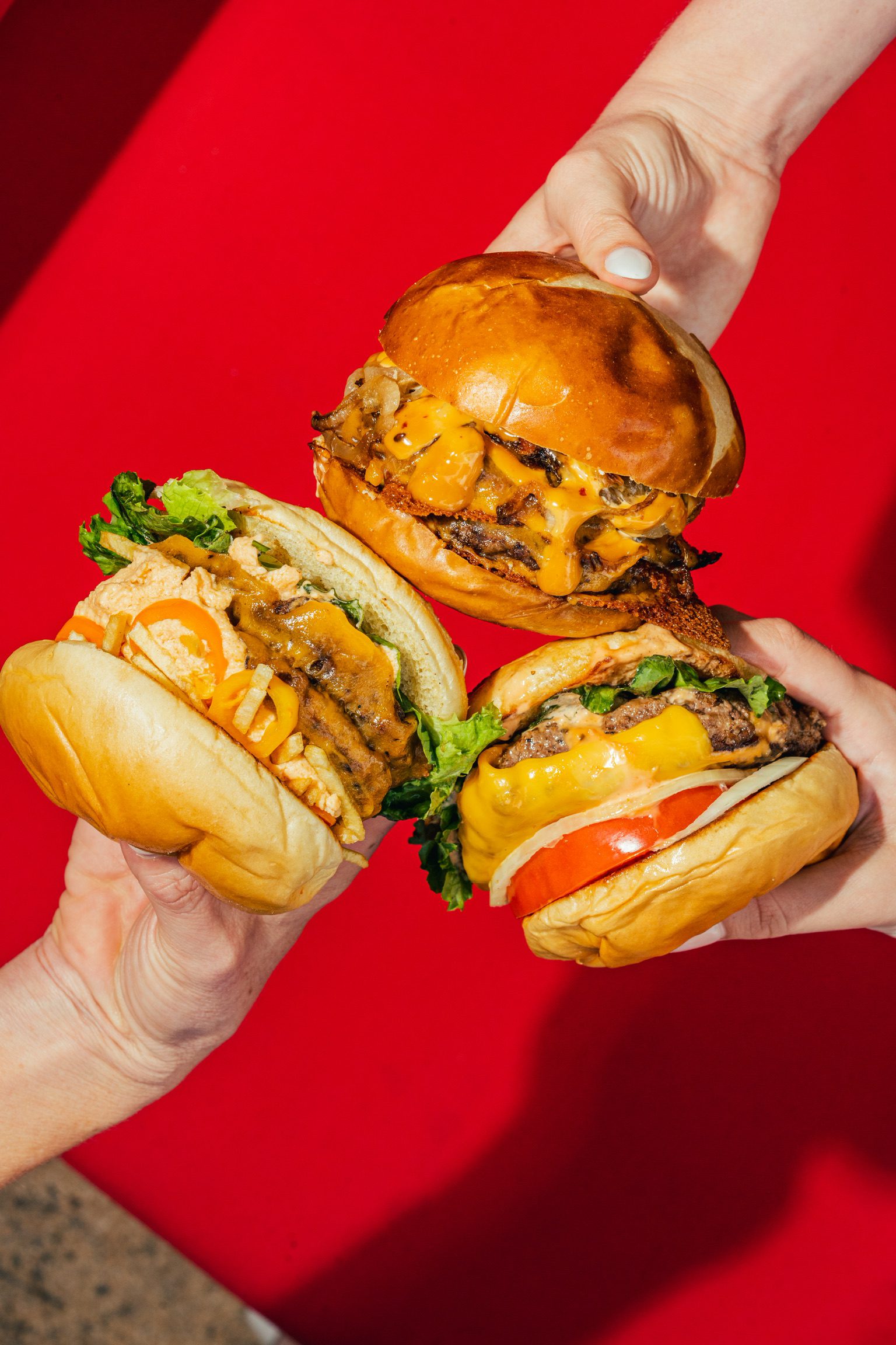Three hands holding three burgers.