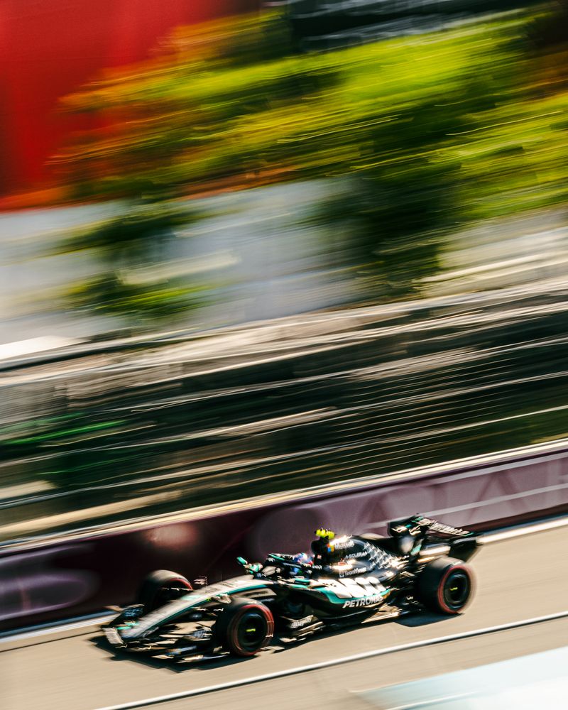 A Formula 1 race car speeds down the track at the F1 Miami Grand Prix, with motion blur highlighting its rapid movement. Trees and barriers in the background blur, emphasizing the car’s incredible velocity.